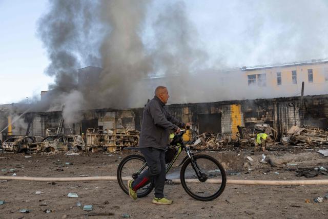 A man carries his bicycle as he past firefighters pushing out a fire following Russian missiles strikes in Kyiv early on September 8, 2026, amid the Russian invasion in Ukraine. A wave of strong explosions rang out in Kyiv, AFP journalists said early on September 8, as Russia resumed strikes on the Ukrainian capital after a three-day halt. (Photo by Serhii Okunev / AFP)