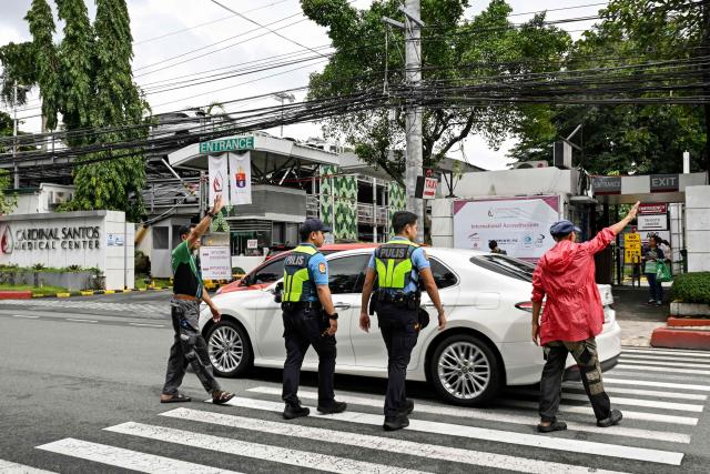 Police cross a street while on patrol outside the Cardinal Santos Medical Center in San Juan, Metro Manila on September 8, 2026, following the arrest of Philippine lawmaker Martin Romualdez, a cousin of President Ferdinand Marcos Jr. Philippine police arrested a lawmaker and cousin of President Ferdinand Marcos Jr. in his hospital bed on September 8 over his alleged involvement in a massive corruption scandal tied to bogus flood control projects. (Photo by Jam STA ROSA / AFP)