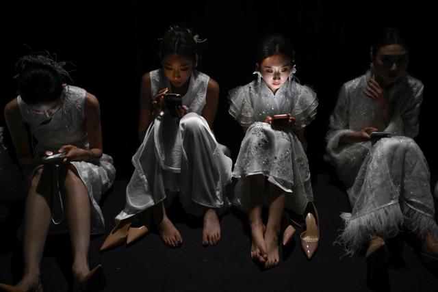 Models use their mobile phones as they wait backstage before presenting creations from the Guanju collection by Guan Yazheng during the China Fashion week in Beijing on September 8, 2026. (Photo by WANG Zhao / AFP)
