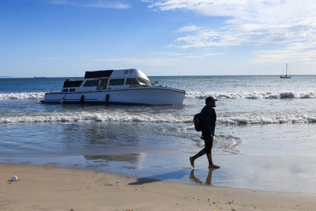 A man walks past a grounded boat that washed up on Playa Del Rey Beach, California, on September 8, 2026. Hurricane Marie stayed well offshore of Southern California during Labor Day weekend but its large swells produced dangerous surf and rip currents, with waves reaching around 10 feet in some areas. (Photo by David Swanson / AFP)