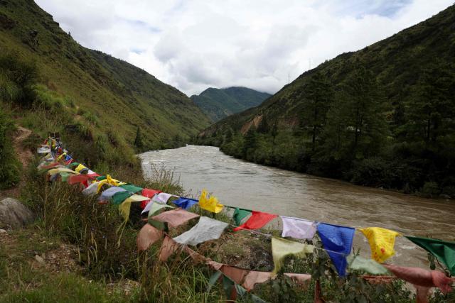 This photograph taken on September 3, 2026 shows Buddhist prayer flags fluttering along the Paro Chuu riverline in Paro, Bhutan. The glacial collapse that caused deadly floods on the Nepal-Tibet border late last month is a stark reminder of the dangers faced by Bhutan, which has over 600 glaciers nestled in the mountain ranges across its north. (Photo by Niharika KULKARNI / AFP)