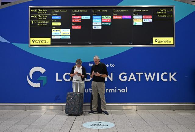 Passengers stand with their luggage underneath an information display board in the South Terminal of London Gatwick airport near Crawley, southern England on September 9, 2026, following second day of major disruption due an issue affecting the NATS air traffic control systems. UK travellers faced more misery on September 9, with more than 150 flights scrapped across the country, as Britain's air traffic control service scrambled to recover from a technical glitch that sparked chaos. (Photo by JUSTIN TALLIS / AFP)