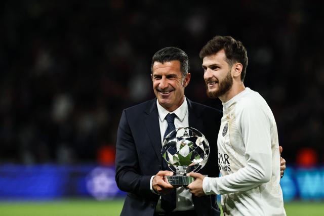 Portuguese former football player and football advisor to UEFA Luis Figo (L) gives Paris Saint-Germain's Georgian forward #07 Khvicha Kvaratskhelia (R) the UEFA Champions League Trophy for best player for the season 2025-2026 prior to the UEFA Champions League, league phase, matchday 1, football match between Paris Saint-Germain (PSG) and Slovan Bratislava at the Parc des Princes Stadium in Paris on September 9, 2026. (Photo by Anne-Christine POUJOULAT / AFP)