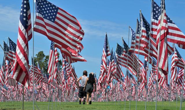 People walk through US flags displayed at Pepperdine University in Malibu, California, on September 9, 2026, as part of the annual Wave of Flags commemorating the September 11, 2001 attacks. (Photo by Frederic J. BROWN / AFP)