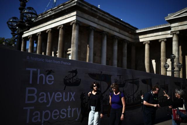 People pass an advertising hoarding, promoting the Bayeux Tapestry exhibition, outside the British Museum in London on September 10, 2026, on the first day of the exhibition. London's sold-out Bayeux Tapestry exhibition opened on September 10 to a British public gripped by "mania" as the medieval artwork depicting the Norman conquest of England goes on display outside France for the first time. (Photo by Henry NICHOLLS / AFP)