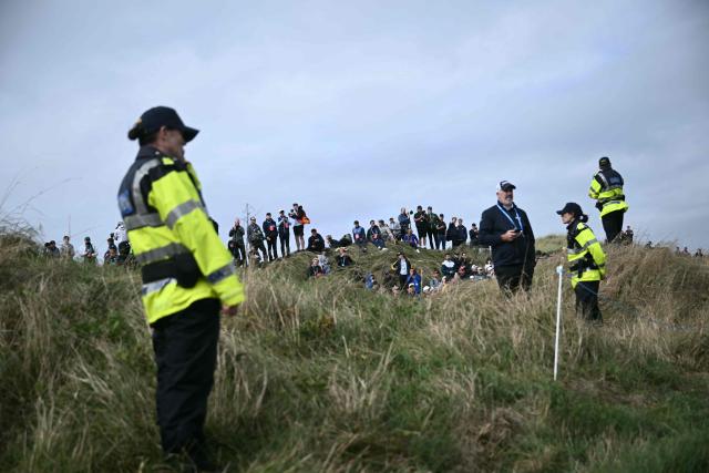 Golf fans look on with members of security ahead of the arrival of US President Donald Trump at the resort and golf course owned by the president in Doonbeg, western Ireland on September 12, 2026, as he visits to attend the Irish Open golf tournament. Trump arrived in Ireland on September 12 for a two-day visit, stopping for a few hours in Dublin before heading west to his Trump International Golf Links to attend the Irish Open. (Photo by Brendan SMIALOWSKI / AFP)