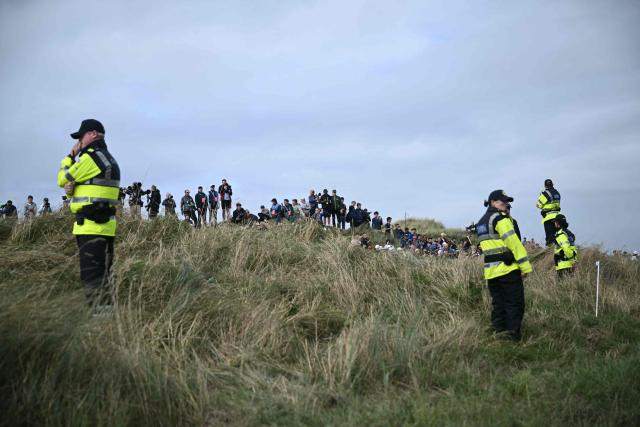 Golf fans look on with members of security ahead of the arrival of US President Donald Trump at the resort and golf course owned by the president in Doonbeg, western Ireland on September 12, 2026, as he visits to attend the Irish Open golf tournament. Trump arrived in Ireland on September 12 for a two-day visit, stopping for a few hours in Dublin before heading west to his Trump International Golf Links to attend the Irish Open. (Photo by Brendan SMIALOWSKI / AFP)