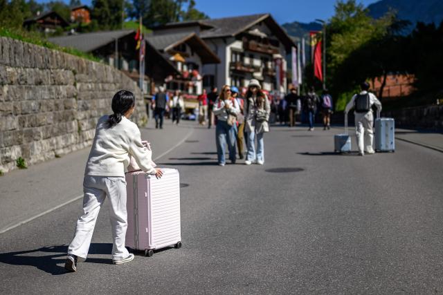 Asian tourists pull their suitcases along a street in the Alpine resort of Grindelwald, Switzerland, on September 12, 2026. (Photo by Fabrice COFFRINI / AFP)
