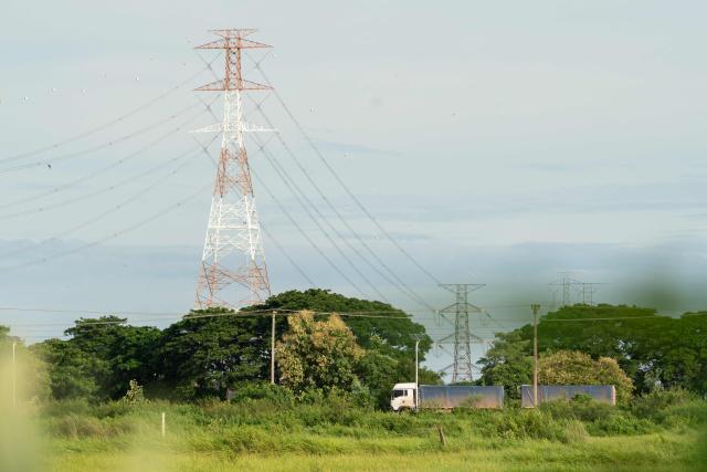 In this photo taken on August 22, 2026, a truck drives past high-voltage transmission lines that cross the Mekong River in Hadxayfong district, Vientiane, as part of the network through which the country exports electricity to neighbouring Thailand. Isolated, under-developed Laos brands itself the "Battery of Southeast Asia", powering its neighbours with dozens of hydroelectric plants, but frequent power outages leave its own people in the dark. (Photo by AFP) / TO GO WITH: Laos-energy-electricity, by Beatrice SIVIERO