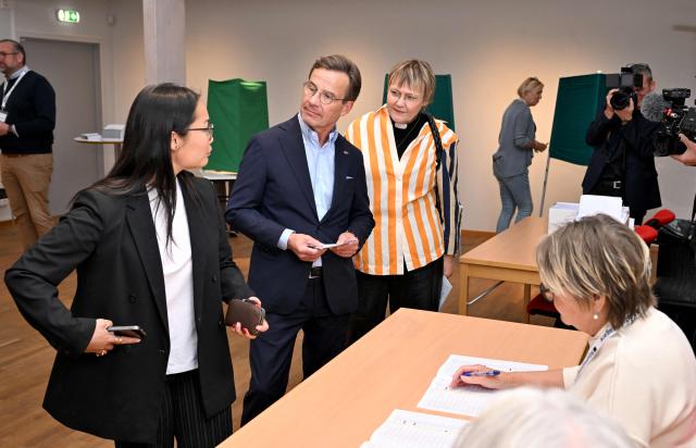 Sweden's Prime Minister Ulf Kristersson (C), leader of the conservative Moderates, stands next to his wife Birgitta Ed (R) and one of their adopted daughters (L) as they get their ballot papers and prepare to cast their ballots at a polling station in Strangnas near Stockholm, during Sweden's general election on September 13, 2026. Polling stations opened on September 13, 2026 in Sweden in what is expected to be a close general election that will see either the far right enter government for the first time or the left-wing opposition reclaim power. (Photo by Jonathan Nackstrand / AFP)