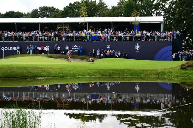 Spectators are reflected in a pond as they look on while US teams golfer Auston Kim (C) lines up a putt during play in her singles match against Team Europe’s English golfer Lottie Woad on the final day of the 2026 Solheim Cup biennial team golf competition on The Bernardus Golf Course at Cromvoirt, some 80kms south-east of Rotterdam on September 13, 2026. (Photo by NICOLAS TUCAT / AFP)