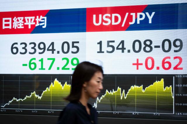 A woman walks past an electronic quotation board displaying the Nikkei Stock Average on the Tokyo Stock Exchange (L) and the foreign exchange rate of the Japanese yen against the US dollar, in Tokyo on September 14, 2026. (Photo by Yuichi YAMAZAKI / AFP)