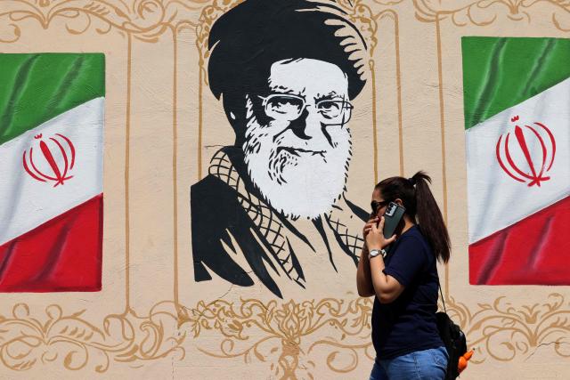 An Iranian woman walks past a wall decorated with the image of assassinated Iranian supreme leader Ayatollah Ali Khamenei and the national flags, in central of Tehran on September 14, 2026. The United States and Israel launched strikes against Iran on February 28, killing Iran's supreme leader and top military leaders, prompting authorities to retaliate with strikes on Israel and across the Gulf. (Photo by ATTA KENARE / AFP) / 