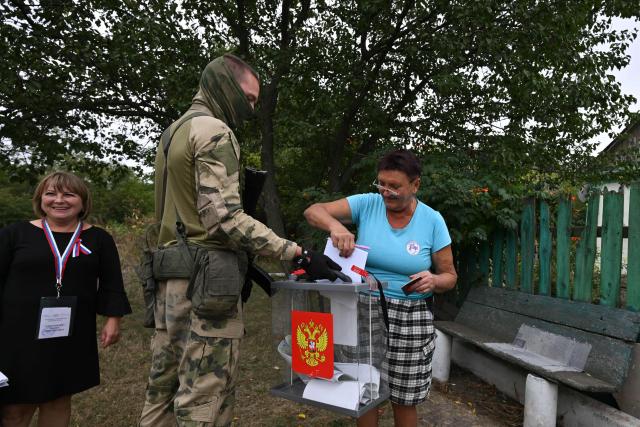 A woman casts her ballot into a mobile ballot box held by a Russian serviceman, who is accompaniyng members of a local election commission, during early voting in Russia's parliamentary election in the settlement of Verbovka in the Donetsk region, Russian-controlled Ukraine, on September 14, 2026, amid the ongoing Russian-Ukrainian conflict. The 2026 parliamentary election will be held over a three-day period from September 18 to 20. (Photo by AFP)