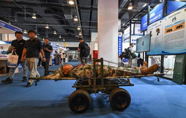 A man (C) lays down on a unmanned ground vehicle for a demonstration during the 14th China International Defence Electronics Exhibition (CIDEX) in Beijing on September 15, 2026. (Photo by ADEK BERRY / AFP)