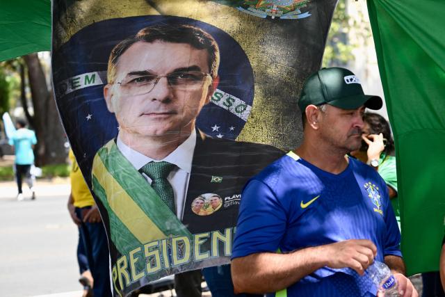 A vendor sells campaign merchandise supporting presidential candidate Flavio Bolsonaro outside the National Congress in Brasilia on September 15, 2026, during a hearing at Brazil's Supreme Federal Court (STF) on the investigation into alleged links between Supreme Court Justice Alexandre de Moraes and banker Daniel Vorcaro. Brazil's Supreme Court on September 15 began examining one of its top justice's ties to a jailed banker, in an unprecedented crisis that has eclipsed the country's presidential election campaign. (Photo by Evaristo Sa / AFP)