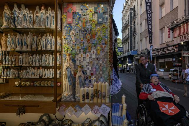 A man pushes a person in a wheelchair past religious items displayed for sale at a shop in Lourdes on September 15, 2026. Pope Leo XIV will travel to Lourdes, a site of pilgrimage for Christians worldwide, where he will hold an open-air mass on Sunday, September 27, before presiding over another at the cathedral in the northeastern city of Metz on September 28. (Photo by Ed JONES / AFP)