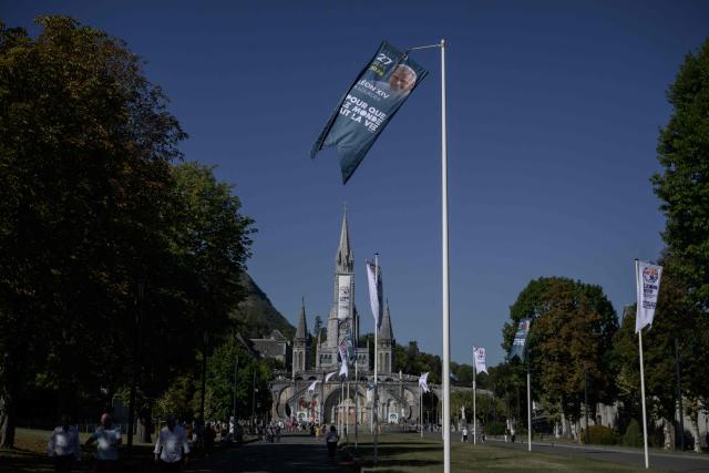 This photograph shows a banner announcing a visit by Pope Leo, with a view of the Basilique Notre-Dame du Rosaire, in Lourdes on September 15, 2026. Pope Leo XIV will travel to Lourdes, a site of pilgrimage for Christians worldwide, where he will hold an open-air mass on Sunday, September 27, before presiding over another at the cathedral in the northeastern city of Metz on September 28. (Photo by Ed JONES / AFP)