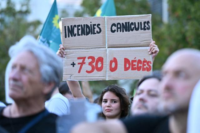 A protester holds a placad reading "wildfires and heatwaves +7300 dead" during a demonstration "to say stop to climate austerity" called by a coalition of 53 organizations ahead of political discussions on an upcoming government budget and finance law near Bercy France's Ministry of the Economy in Paris on September 15, 2026. (Photo by LOU BENOIST / AFP)