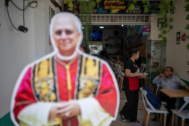 A worker serves customers at a restaurant specializing in traditional Chiclayo cuisine in Lima on September 15, 2026, as a life-size cutout depicting the pontiff stands in the foreground. Pope Leo XIV will visit Uruguay, Argentina and Peru from November 6 to 17, the Vatican said on August 5, in a return to the continent where the pontiff spent decades as a missionary. (Photo by Ernesto BENAVIDES / AFP)