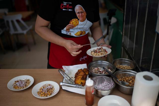 A worker serves dishes at a restaurant specializing in traditional Chiclayo cuisine in Lima on September 15, 2026, while wearing a T-shirt depicting Pope Leo XIV holding "Tortitas de Choclo.". Pope Leo XIV will visit Uruguay, Argentina and Peru from November 6 to 17, the Vatican said on August 5, in a return to the continent where the pontiff spent decades as a missionary. (Photo by Ernesto BENAVIDES / AFP)