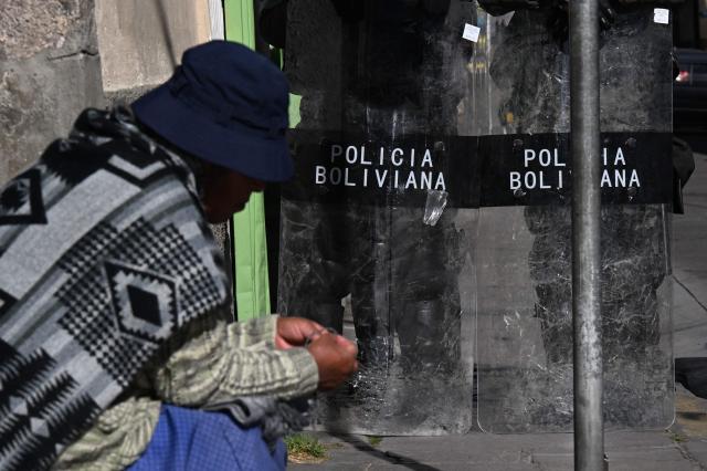 A man sits next to Bolivian riot police officers standing guard in a protest by education workers against the national government in La Paz on September 15, 2026. (Photo by Aizar RALDES / AFP)