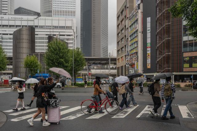 People use umbrellas to shelter themselves from the rain while crossing a road in Nagoya on September 16, 2026. (Photo by Mohd Rasfan / AFP)