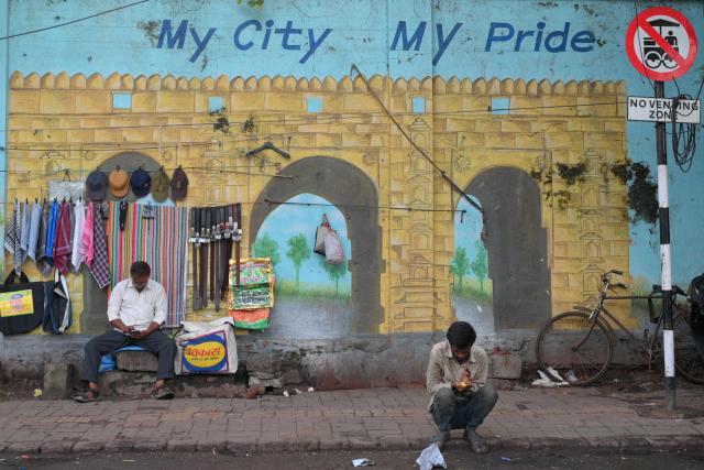 A vendor waits for customers in front of a mural along a road in Ahmedabad on September 16, 2026. (Photo by Shammi MEHRA / AFP)