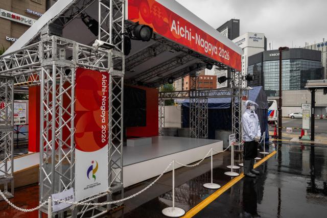 A man wearing a rain jacket stands in front of a booth promoting the 2026 Asian Games in Nagoya, Aichi Prefecture on September 16, 2026. (Photo by Mohd Rasfan / AFP)