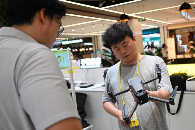 An employee (R) at a drone reception module at a shopping mall inspects a drone brought in by its owner in Beijing on September 16, 2026. Authorities in Beijing have set up official points for residents to hand in their unmanned aircraft before November 15, when a total ban on possessing, storing and flying drones citywide takes effect. Owners can choose a government-subsidized buyback or recycling. (Photo by Pedro PARDO / AFP)