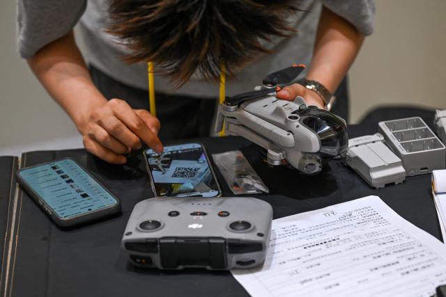 An employee at a drone reception module in a shopping mall inspects a drone brought in by its owner in Beijing on September 16, 2026. Authorities in Beijing have set up official points for residents to hand in their unmanned aircraft before November 15, when a total ban on possessing, storing and flying drones citywide takes effect. Owners can choose a government-subsidized buyback or recycling. (Photo by Pedro PARDO / AFP)