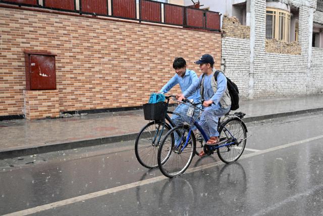 Afghan school boys ride bicycles along a road during a rain shower in Kabul on September 16, 2026. (Photo by Wakil KOHSAR / AFP)