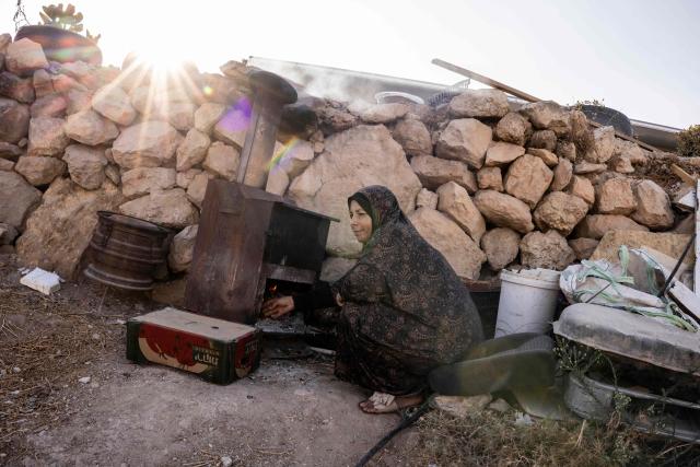 Fatma Amr stokes the fire in her oven while baking cakes outside the cave that her family has turned into their home in the village of Al-Tuwani, in the Israeli-occupied West Bank, on September 11, 2026. After his home was destroyed by Israeli forces in 2023, Mohammed Fadel Amr took shelter in caves, where he now lives with his two wives, Fatma Amr and Arwa Amr, and their eleven children. Mohammed and his family say they face almost daily harassment from settlers living in a nearby illegal Israeli settlement outpost. At the end of August 2026, Israeli forces reportedly ransacked the family's makeshift home during a night raid, and settlers later stole his goats, depriving him of his livelihood. (Photo by John WESSELS / AFP)