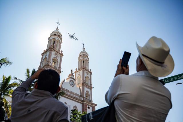 A man takes snapshots of a helicopter during  the Independence Day military parade in Culiacan, state of Sinaloa, Mexico, on September 16, 2026. (Photo by Jesus Verdugo / AFP)