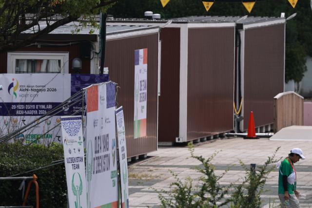 A man walks past temporary wooden container huts being used to house athletes for the 2026 Asian Games at the Garden Pier in Nagoya on September 17, 2026. (Photo by DAVID GRAY / AFP)