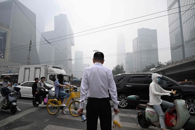A man waits to cross a road on a polluted day in Beijing on September 17, 2026. (Photo by GREG BAKER / AFP)