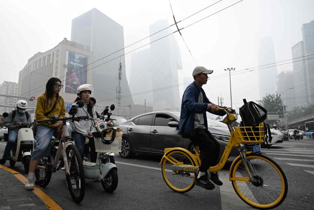 People wait to cross a road on a polluted day in Beijing on September 17, 2026. (Photo by GREG BAKER / AFP)