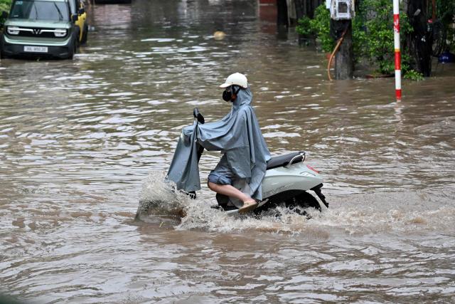 A woman rides an electric scooter along a flooded street in Hanoi on September 17, 2026. (Photo by Nhac NGUYEN / AFP)