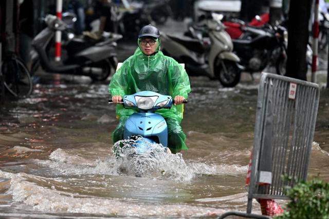 A woman rides a scooter along a flooded sidewalk in Hanoi on September 17, 2026. (Photo by Nhac NGUYEN / AFP)