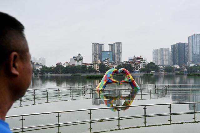 A man looks at a shaped hands sculpture in a flooded recreation area in Hanoi on September 17, 2026. (Photo by Nhac NGUYEN / AFP)