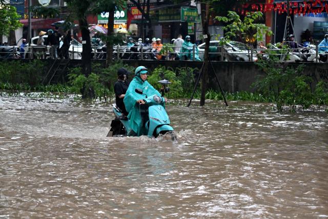 A ride-hailing driver transports a passenger on an electric scooter along a flooded street in Hanoi on September 17, 2026. (Photo by Nhac NGUYEN / AFP)
