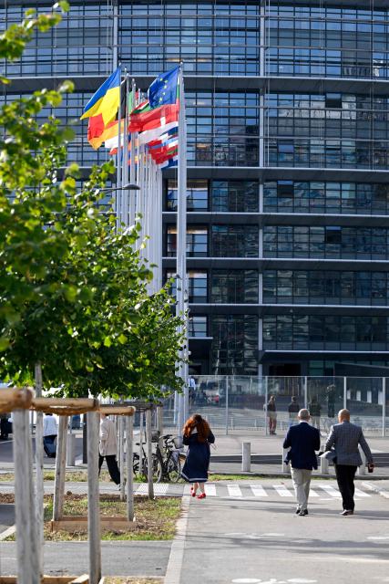 Pedestrians walk past the European flag surrounded by the national flags of the EU member states flapping in the breeze in front of the Louise Weiss building, headquarters of the European Parliament, in Strasbourg, eastern France on September 17, 2026. (Photo by Jean-Christophe VERHAEGEN / AFP)