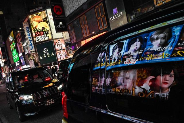 (FILES) This photo taken on March 31, 2025 shows advertisements for entertainment clubs reflected in the window of a passing car, along a street in the red-light entertainment area of Kabukicho in the Shinjuku district of Tokyo. Japan should overhaul its prostitution law to punish those who seek to buy sex, experts recommended on September 17, 2026 in proposals likely to lead to changes to the decades-old legislation. (Photo by Richard A. Brooks / AFP)