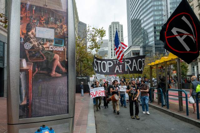 Protesters during a "Stop the AI Race" demonstration calling for a slowdown in the development of advanced artificial intelligence systems pass an advert for AI on Market Street in San Francisco, California, on September 17, 2026. The world's biggest AI companies are working on creating a standards body, ChatGPT-maker OpenAI said on September 15, as fears rise about the dangers of AI and pressure is on to create a safer version of the technology. US President Donald Trump has dismissed warnings about the risks of AI as "hoaxes." (Photo by Karl Mondon / AFP)