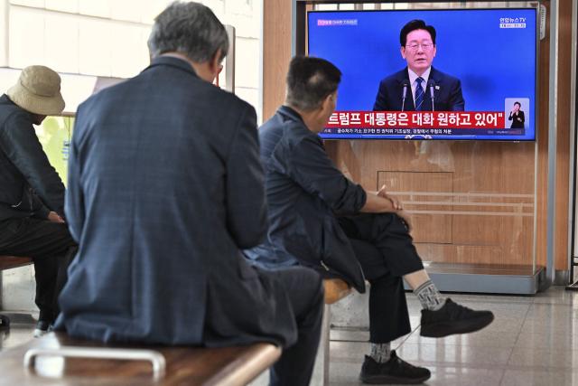 People watch a television screen showing a news broadcast of South Korean President Lee Jae-Myung holding a press conference at the Blue House, at a train station in Seoul on September 18, 2026. (Photo by Lillian SUWANRUMPHA / AFP)