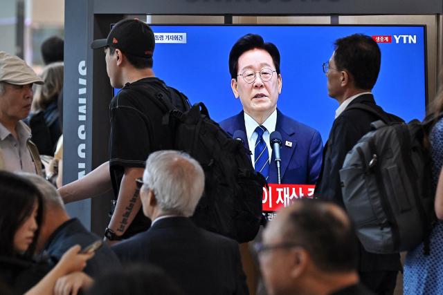 People walk by a television screen showing a YTN news broadcast of South Korean President Lee Jae-Myung holding a press conference at the Blue House, at a train station in Seoul on September 18, 2026. (Photo by Lillian SUWANRUMPHA / AFP)