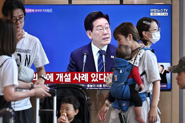 People gather near a television screen showing a Yonhap news broadcast of South Korean President Lee Jae-Myung holding a press conference at the Blue House, at a train station in Seoul on September 18, 2026. (Photo by Lillian SUWANRUMPHA / AFP)