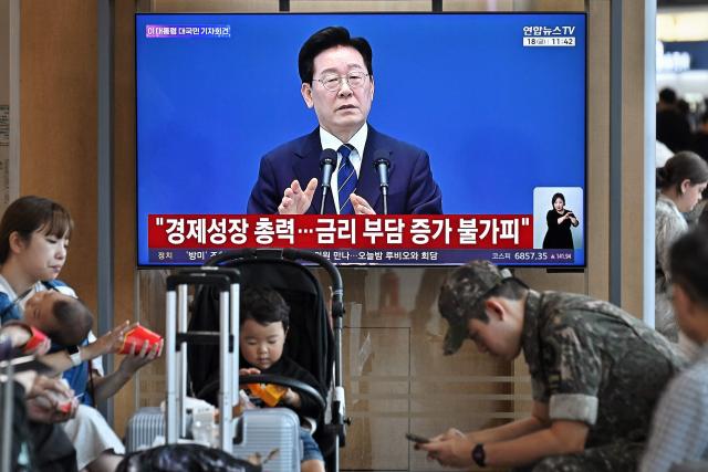People sit near a television screen showing a Yonhap news broadcast of South Korean President Lee Jae-Myung holding a press conference at the Blue House, at a train station in Seoul on September 18, 2026. (Photo by Lillian SUWANRUMPHA / AFP)