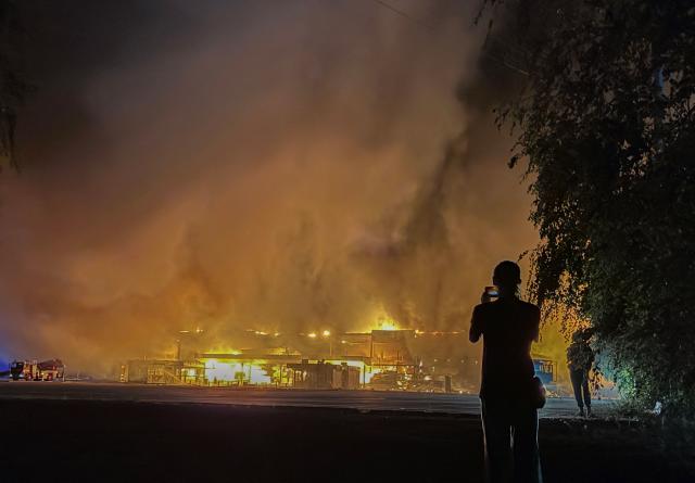 A local resident takes a picture of a burning mall following a drone strike in Zaporizhzhia, late on September 17, 2026, amid the Russian invasion of Ukraine. (Photo by Darya NAZAROVA / AFP)