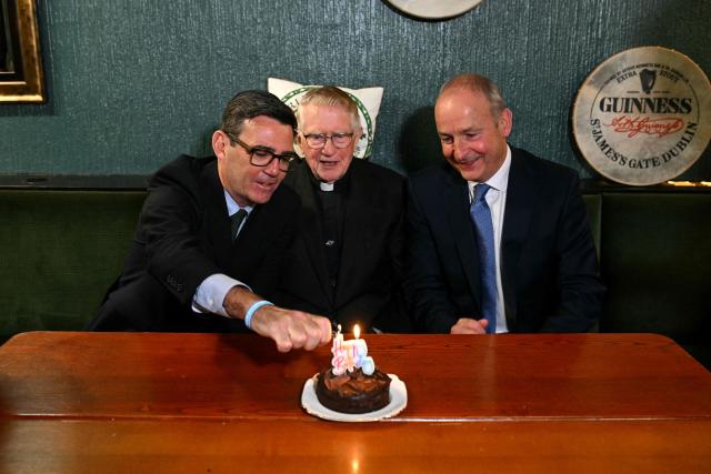 Britain's Prime Minister Andy Burnham (L) lights a candle on the birthday cake for Canon Patrick J MacNally alongside Ireland's Prime Minister Micheal Martin (R) during a visit to the Brian Boru Irish Club in, Ashton-in-Makerfield, northern England, on September 18, 2026. (Photo by Oli SCARFF / POOL / AFP)